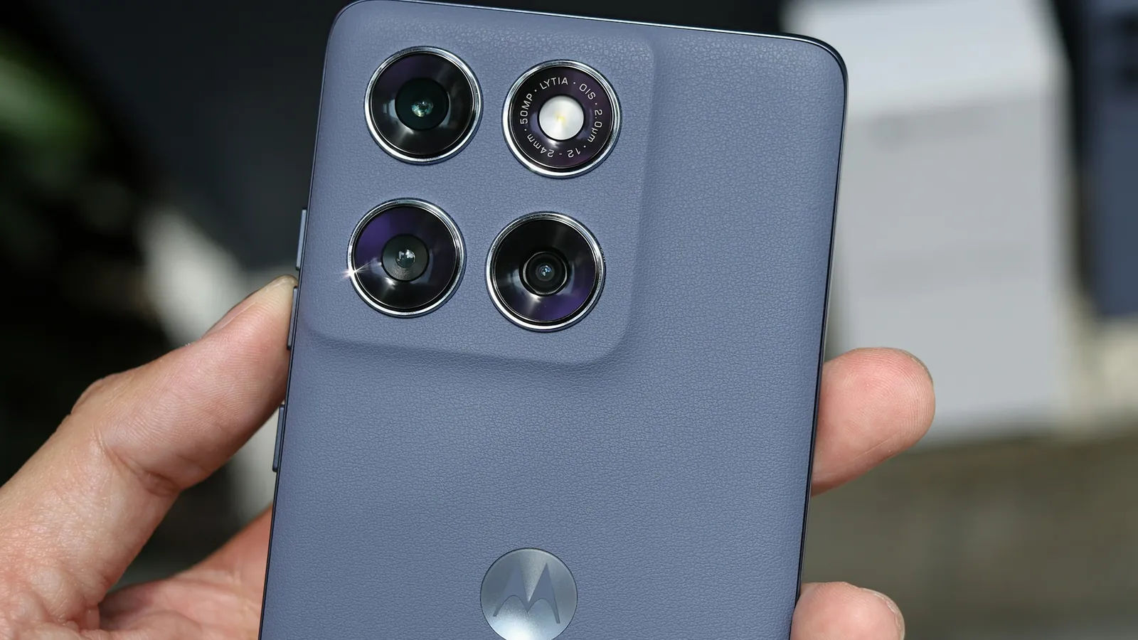 Hand holding a grey Motorola smartphone with a four-camera array
